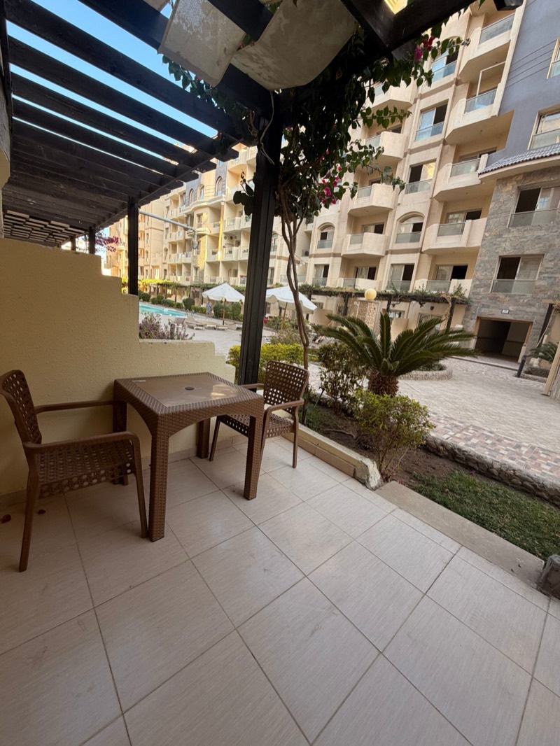 The terrace under its wooden pergola, a table for two, and the pool in the gardens behind